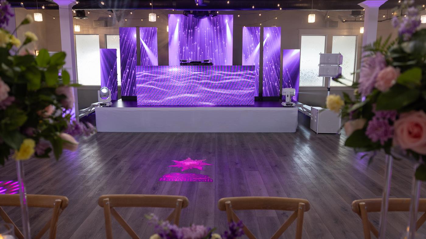 Bar mitzvah stage in a Las Vegas venue — a split LED video wall in purple with white line array speakers and white moving-head fixtures